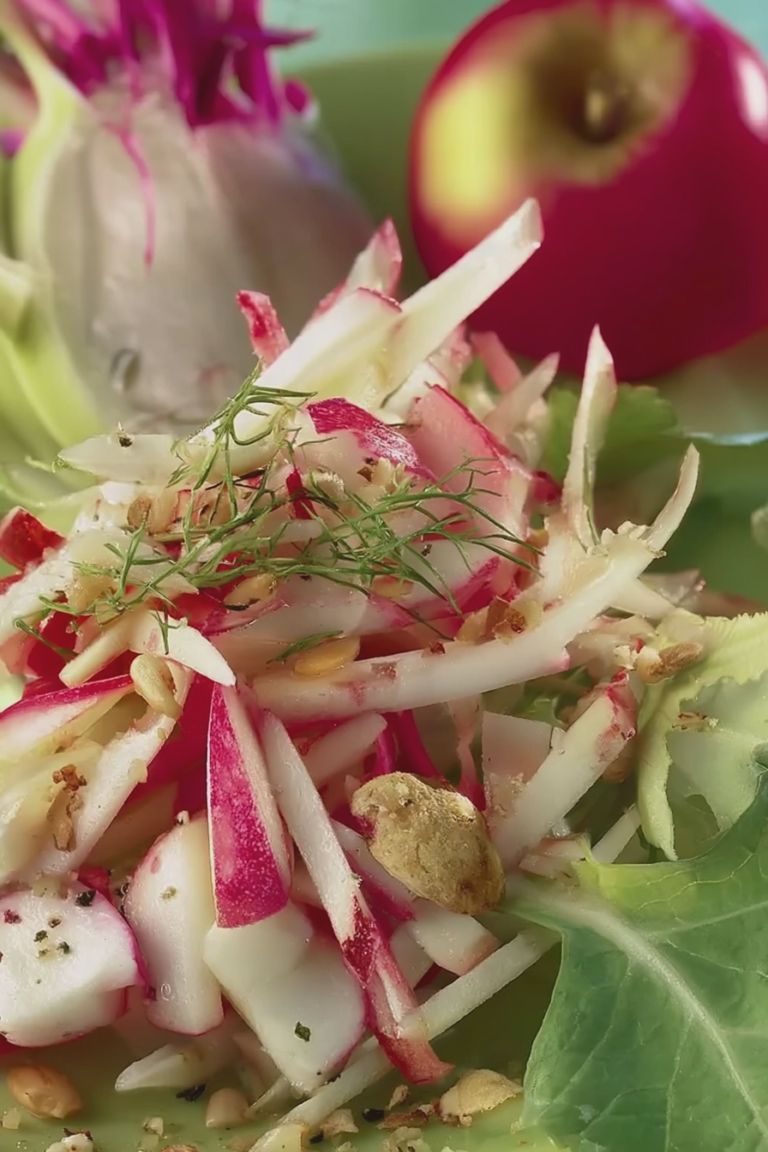 Frischer Apfel-Kohlrabi-Salat mit Minze und Radieschen auf einem Holztisch.